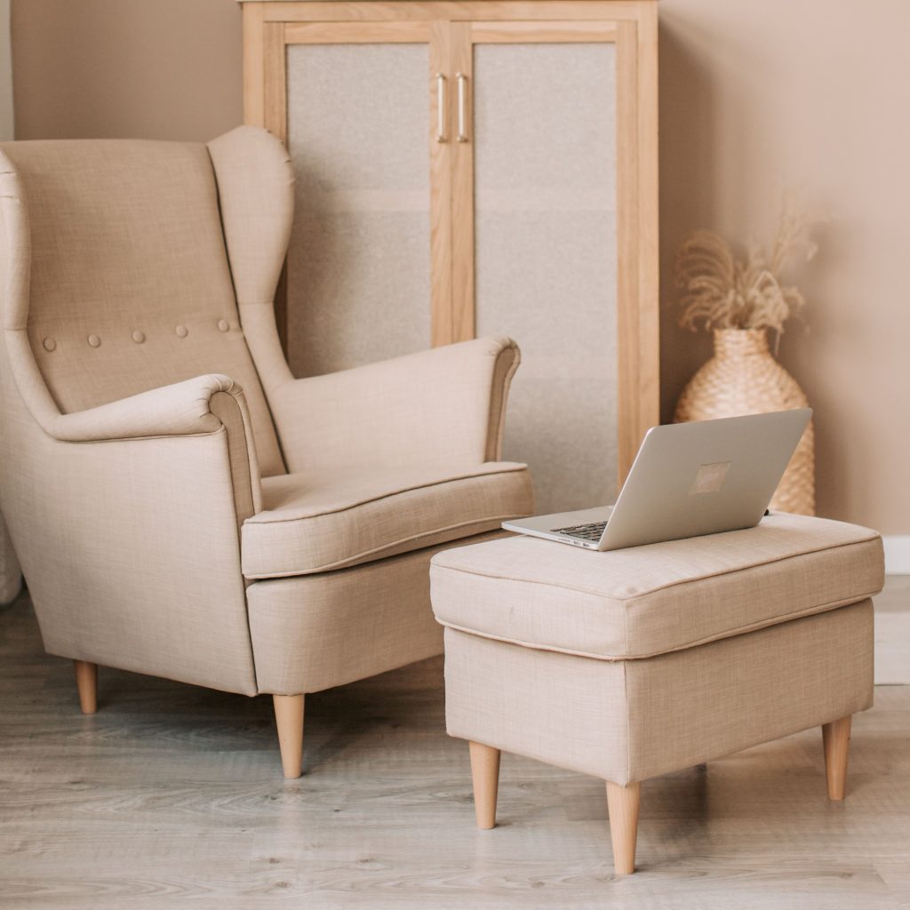 Poltrona e poggiapiedi beige con un portatile, in un soggiorno dallo stile minimalista.