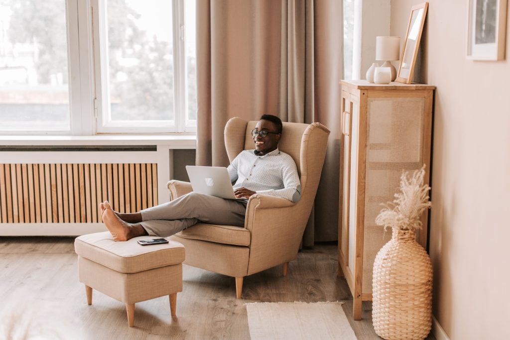 Un uomo si rilassa a casa con un portatile, godendosi una postazione di lavoro da remoto moderna e confortevole.
